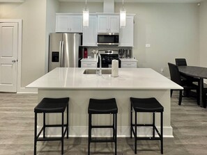 A modern kitchen with white cabinets, stainless steel appliances, and a central island with bar stools.