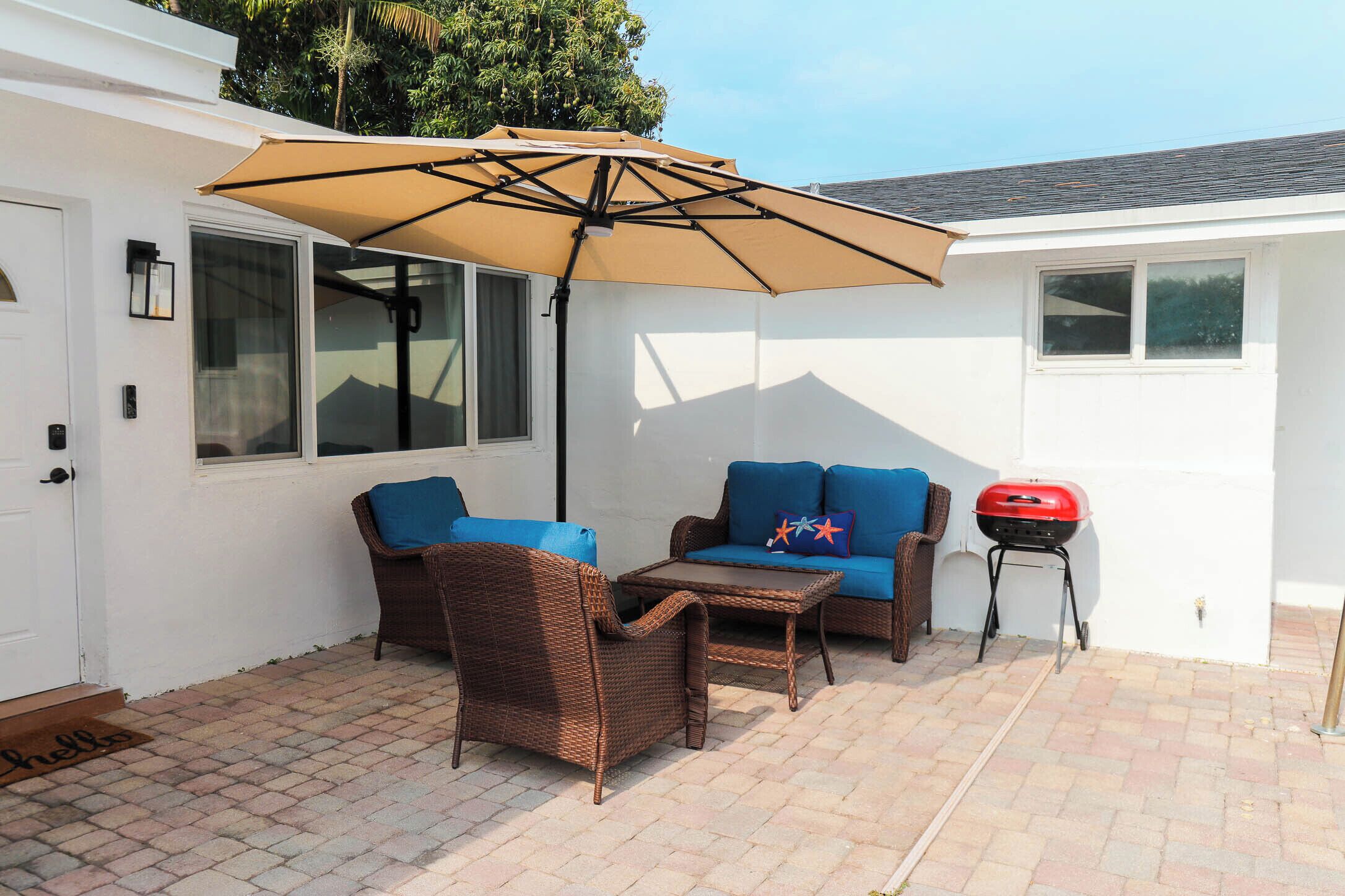 An outdoor patio with wicker furniture, a barbecue grill, and a large umbrella.