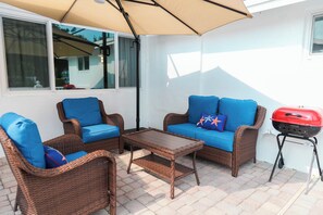 A patio with wicker furniture, a grill, and a window. - Social  Studio · Pool · Beach · FLL Airport · Hard Rock · FIFA 2026 · Sleeps 3 (Fort Lauderdale)