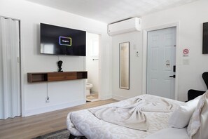 Une chambre moderne équipée d’un lit, d’un téléviseur fixé au mur, d’un climatiseur fixé au mur et d’une porte sur laquelle est apposé un panneau « interdiction de fumer ».