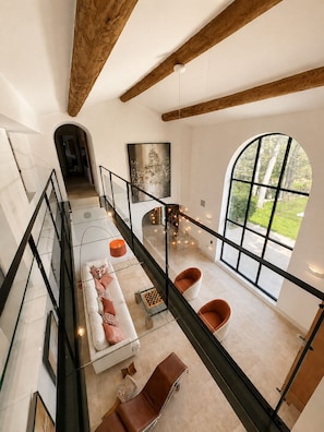 A spacious loft with high ceilings, exposed wooden beams, a large arched window, and a modern interior design. - Charming villa in the heart of a golf estate between Luberon and Alpilles (Mallemort)