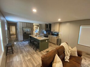 A modern kitchen with a central island, bar stools, a refrigerator, and a microwave.