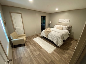A bedroom with a bed, a chair, a rug, and a wall with a sign.
