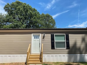 A single-story mobile home with a front door, a small window with shutters, and a wooden front porch.