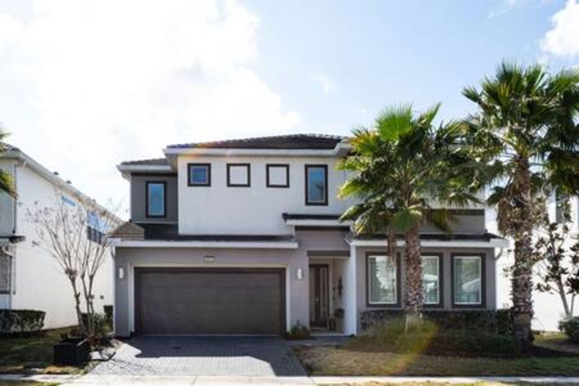 A modern two-story house with a garage, a driveway, and palm trees.