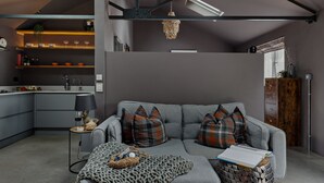 Een moderne woonkamer met een grijze bank, geruite kussens, een gebreide plaid en een bijzettafeltje met een lamp.