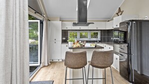 Eine moderne Küche mit einer zentralen Kochinsel, zwei Barhocker und einem großen Fenster.