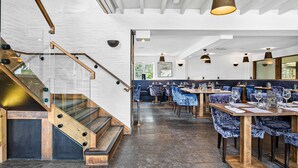 Ein modernes Restaurant mit einer Holztreppe, dunklen Fliesenböden und blau gepolsterten Stühlen.