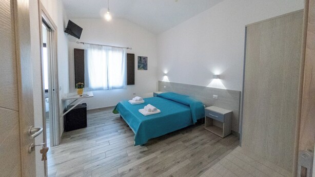 A bedroom with a bed, bedside tables, a desk, a chair, a window with curtains, and a wall-mounted TV. - Lovely guesthouse 10 minutes from the beautiful beaches of the Gulf of Orosei (Irgoli)