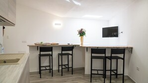 A kitchen with a wooden countertop, two black bar stools, a vase with flowers, and a flat-screen TV mounted on the wall. - Lovely guesthouse 10 minutes from the beautiful beaches of the Gulf of Orosei (Irgoli)