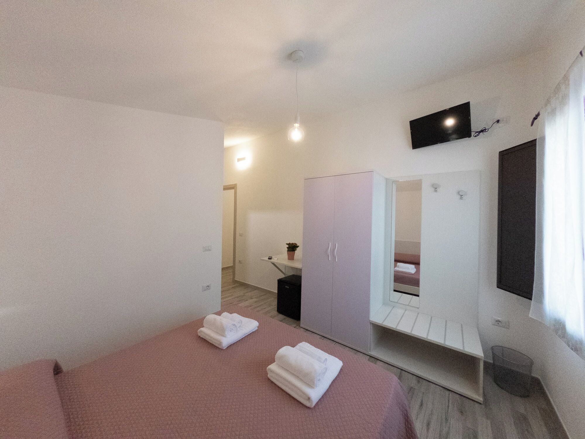 Hotellihuone, jossa on sänky, vaatekaappi, televisio ja kylpyhuone.