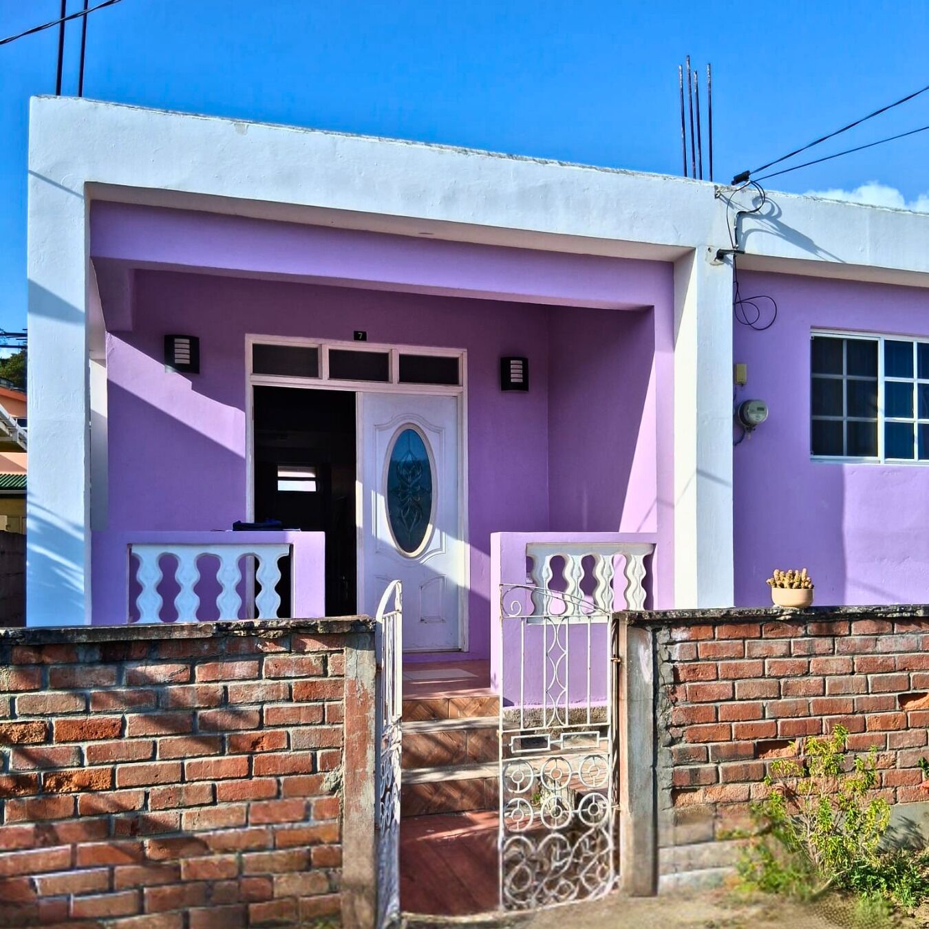 A two-story building with a purple facade, a white door, and a metal gate.