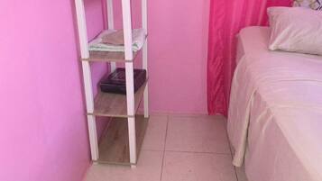 Une chambre avec un lit, une étagère blanche et une fenêtre ornée de rideaux roses.
