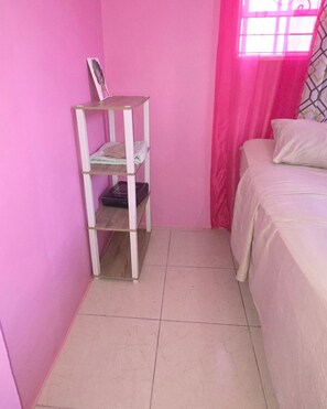 Un dormitorio con una cama, un estante blanco y una ventana con cortinas rosadas.