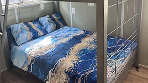 A bunk bed with a blue and gold patterned bedspread, metal railings, and a window with a view. - The Fishin’ Shack, on Lake whitney. (Clifton)