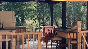 An outdoor wooden deck with a covered seating area, a grill, and a rustic chair. - The Fishin’ Shack, on Lake whitney. (Clifton)