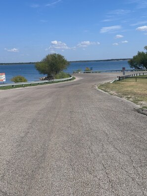 A paved road curving around a body of water with a no parking sign, a grassy area, and a metal railing along the edge.
