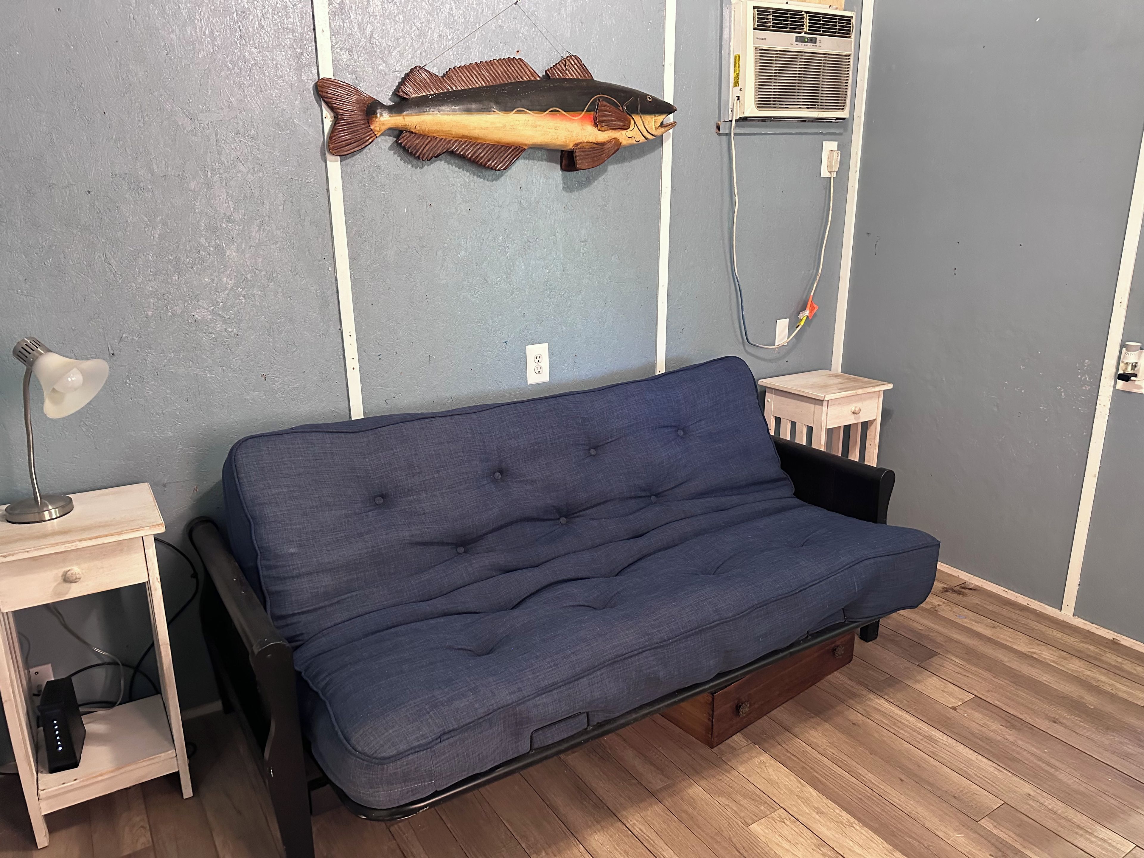 A room with a blue sofa, a small wooden side table, a lamp, and a wall-mounted fish decoration.