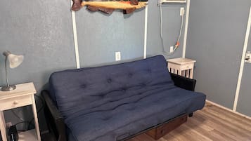 A room with a blue sofa, a small wooden side table, a lamp, and a wall-mounted fish decoration.