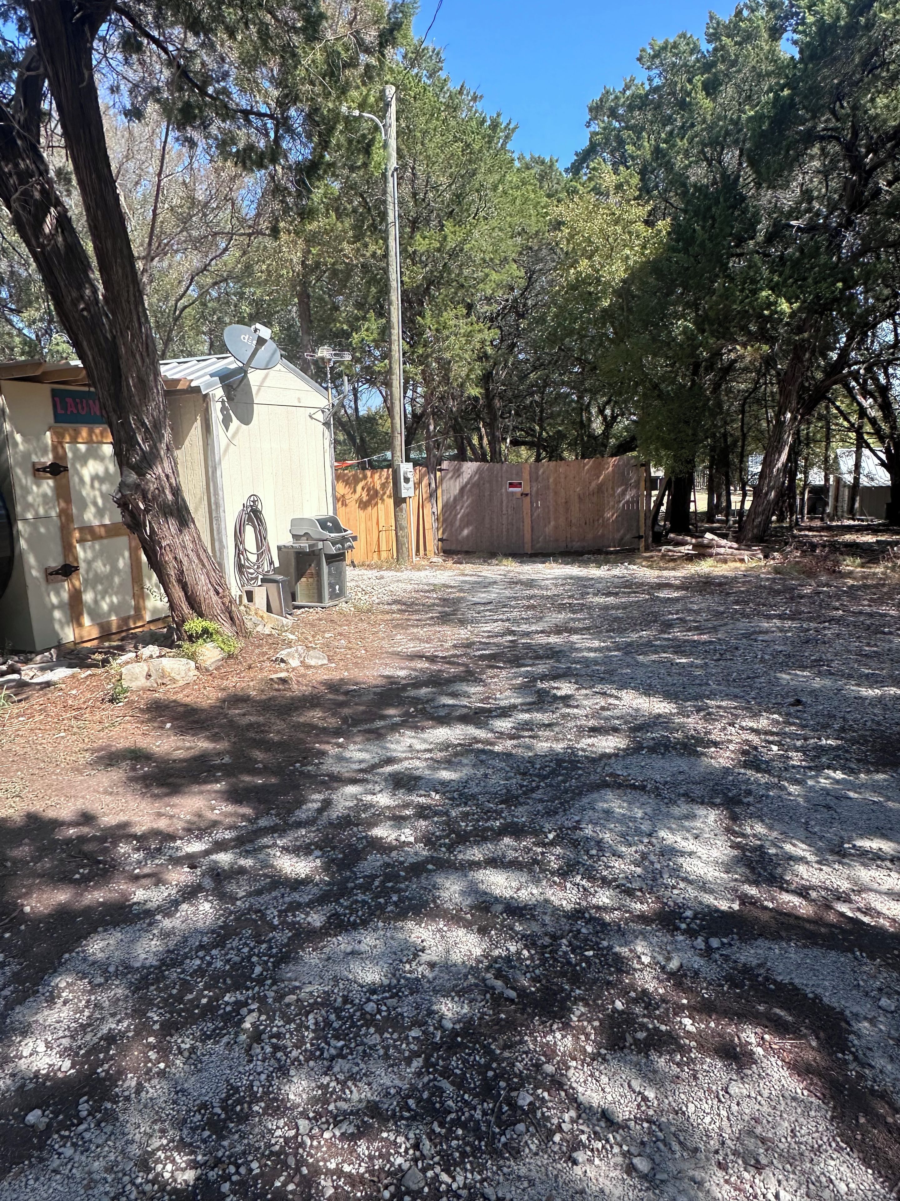 A fenced yard with a gravel driveway, a shed, and a satellite dish.