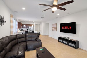 Ein modernes Wohnzimmer mit Ecksofa, Couchtisch, Fernseher und Deckenventilator.