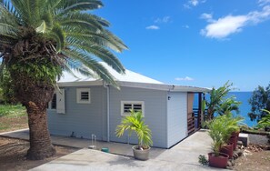 Een gelijkvloers huis met een witte gevel, een betonnen veranda en uitzicht op de oceaan.