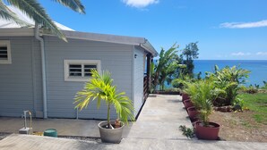 A house with a concrete pathway leading to a door, surrounded by potted plants and a view of the ocean. - Ti Kaz Robin (Trois-Rivières)