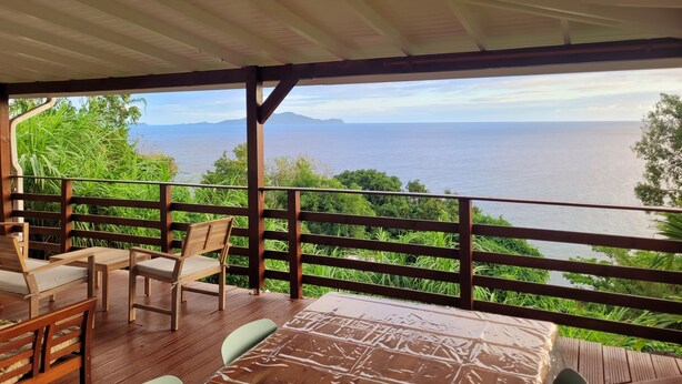 A covered outdoor seating area with wooden furniture and a view of the sea. - Ti Kaz Robin (Trois-Rivières)