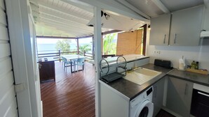A compact kitchen with a washing machine, a sink, and a dining area with a table and chairs. - Ti Kaz Robin (Trois-Rivières)