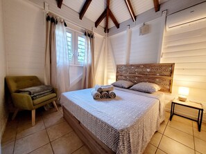 Een slaapkamer met een bed, een stoel, een nachtkastje en een raam met gordijnen.
