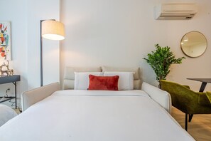A hotel room with a bed, a lamp, a mirror, a plant, and a desk. - Premium Living | Rooftop +Underground Parking (Montreal)