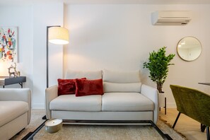 A modern living room with a sofa, a floor lamp, a round mirror, a potted plant, and a side table with a candle. - Premium Living | Rooftop +Underground Parking (Montreal)