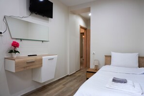 Ein Hotelzimmer mit Bett, Nachttisch, Spiegel, Wand-Fernseher und einem Holztisch mit Schublade.