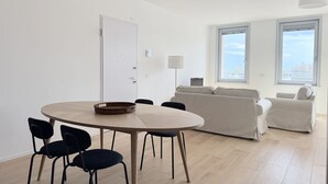 Moderni olohuone, jossa on pyöreä puinen pöytä, mustat tuolit, beigen värinen sohva ja lamppu.