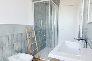 Ein modernes Badezimmer mit einer in Glas abgeschlossenen Dusche, einem weißen Waschbecken und einer Holzleiter.