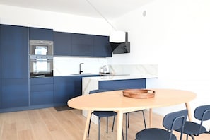 Eine moderne Küche mit dunkelblauer Schränken, einem eingebauten Backofen und einem runden Holztisch mit Stühlen.
