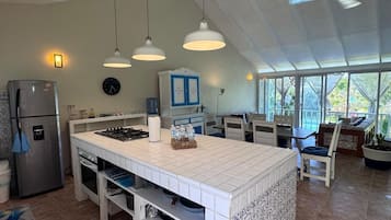 Una cocina amplia con una isla grande, luces colgantes, un refrigerador y un comedor con sillas y una mesa.