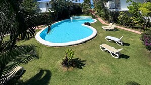 A swimming pool with lounge chairs, surrounded by palm trees and a clear blue sky. - Spacious 3-bedroom condo in adorable Las Terrenas with AC (Las Terrenas)
