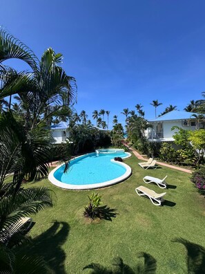 A swimming pool with lounge chairs, surrounded by palm trees and a clear blue sky. - Spacious 3-bedroom condo in adorable Las Terrenas with AC (Las Terrenas)