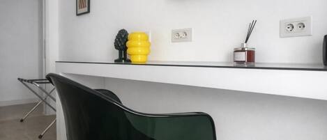 Eine moderne Küche mit einem schwarzen Stuhl, einer weißen Arbeitsplatte, einem darüber montierten Fernseher und einem gelben Dekorationsobjekt auf der Arbeitsplatte.