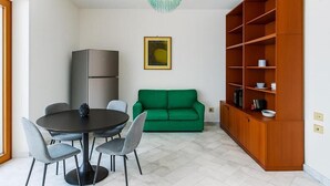 Un espacio habitable compacto con una mesa de comedor, sillas, un sofá verde, una estantería de madera y una lámpara moderna.