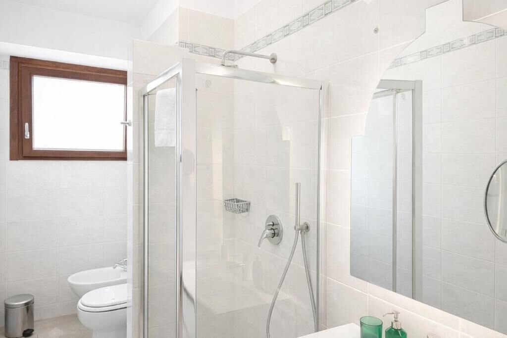A modern bathroom with a glass-enclosed shower, a toilet, and a sink with a mirror.