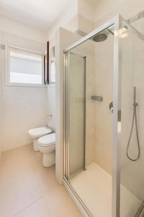 A modern bathroom with a glass-enclosed shower, a toilet, and a window. - roof and sky (Sorrento)