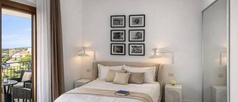 Un dormitorio con cama, un balcón con mobiliario exterior y cuadros en la pared.