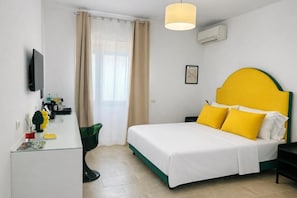 Hotellihuone, jossa on sänky, työpöytä, tuoli, televisio, ikkuna verhoilla ja ilmastointilaite.