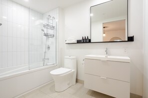 Un baño moderno con ducha envuelta en vidrio, inodoro, tocador con espejo y estante con artículos de aseo.
