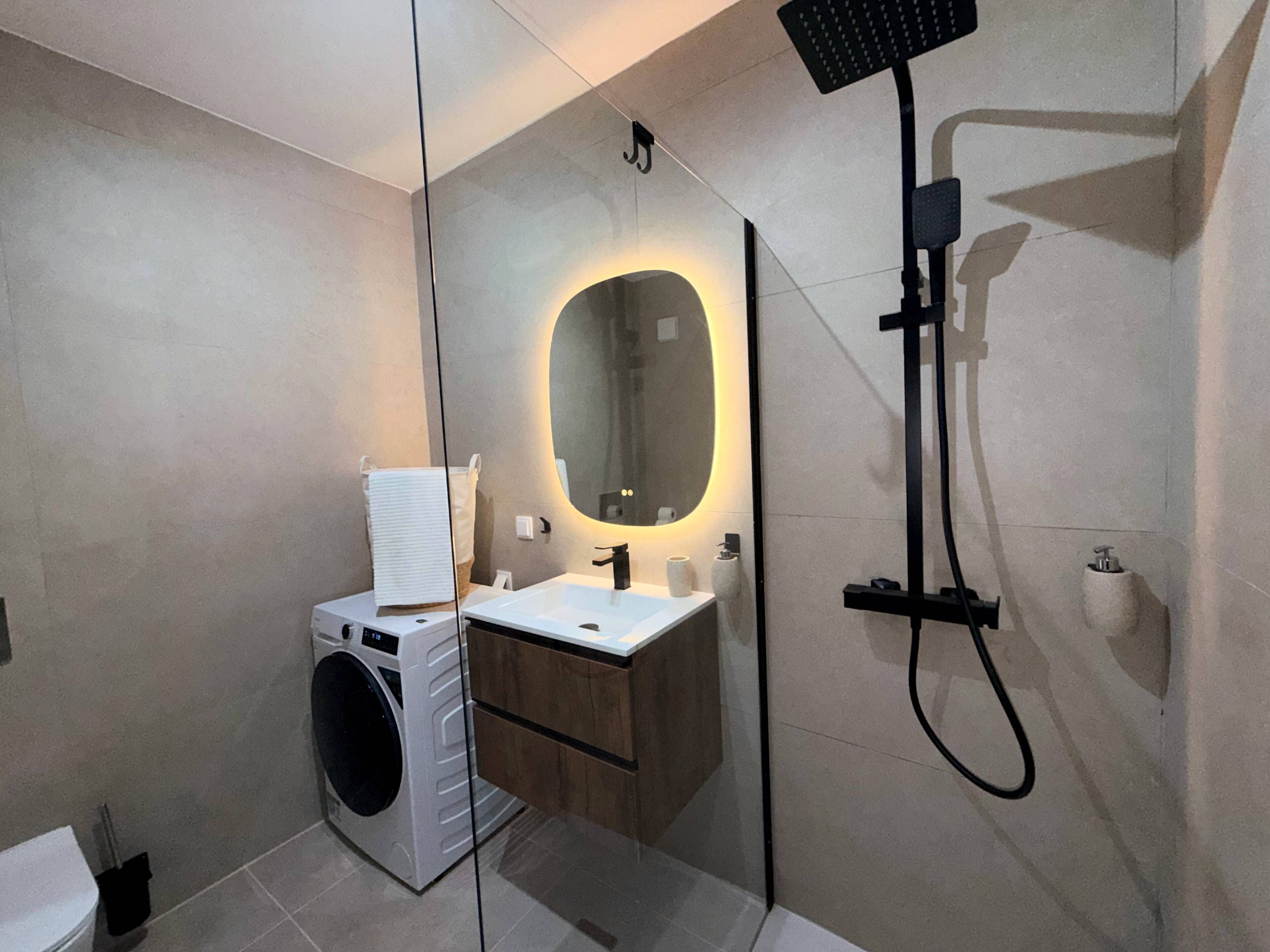 Ein modernes Badezimmer mit Waschmaschine, Waschbecken und Dusche.