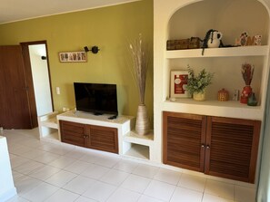 A living room with a television on a stand, a wooden cabinet, a shelf with decorative items, and a door leading to another room. - Authentic apartment, 2 lovely private balconies (Albufeira)