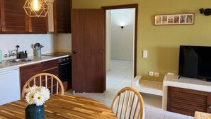 Une cuisine avec des meubles en bois, une table à manger avec des chaises, un téléviseur et un couloir menant à une autre pièce.