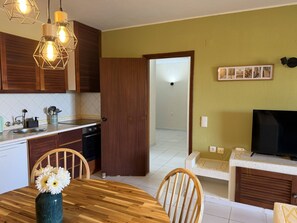 A kitchen with wooden cabinets, a dining table with chairs, a TV, and a hallway leading to another room. - Authentic apartment, 2 lovely private balconies (Albufeira)